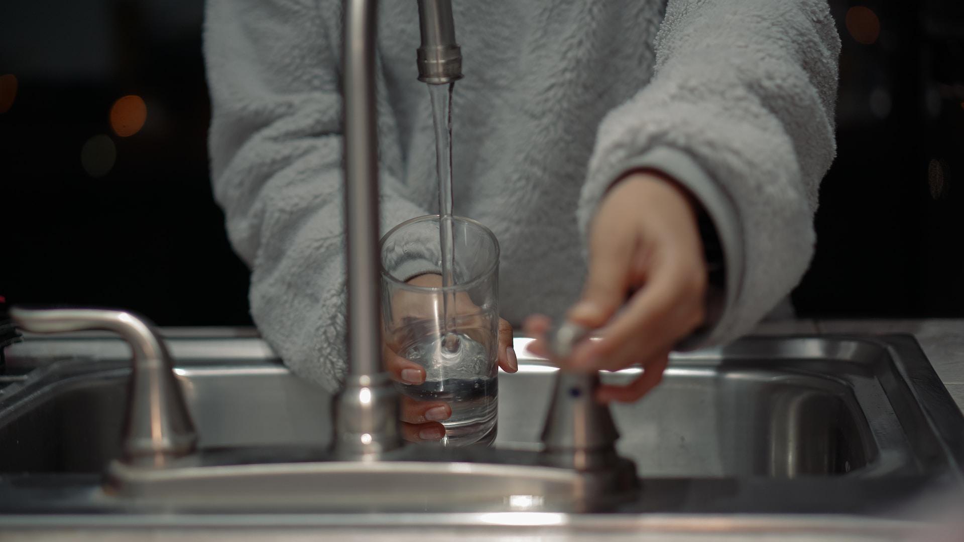 person pouring a glass of water from a tap